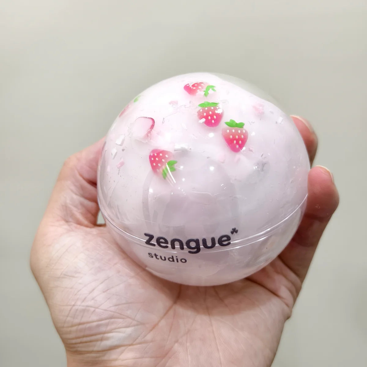 Hand holding a pale pink strawberry-decorated ZENGUE sensory ball in its branded packaging